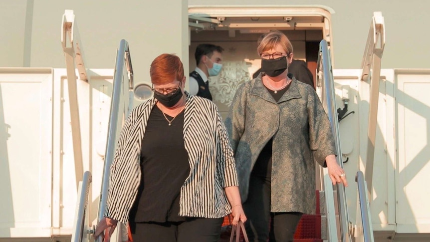 two women with black masks walking down red stairs