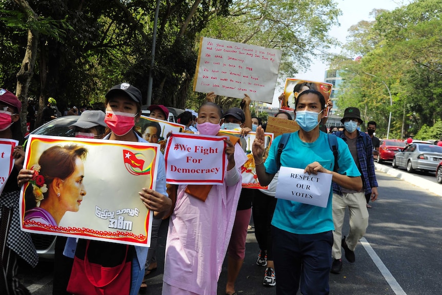 Protesters wearing face masks march along a road holding signs reading "respect out values" and "we fight for democracy".
