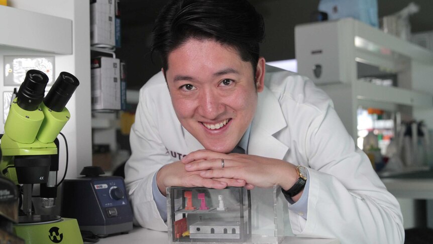 Dr Joshua Chou resting his hands and head on a box-shaped prototype of the device that will take the cancer cells into space