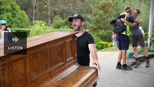 Kelvin Smith pushing an upright piano past a park. Has Audio.