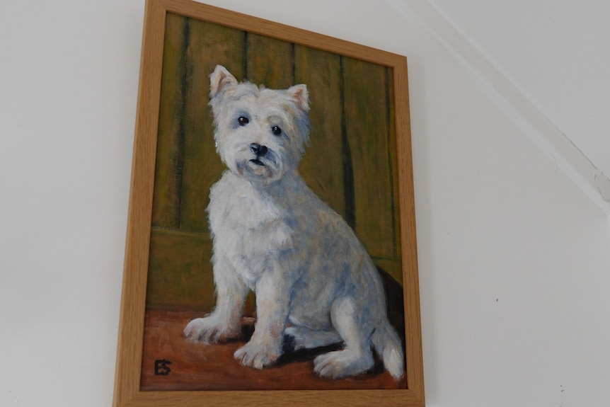 A painting of a white dog hanging on a white wall.