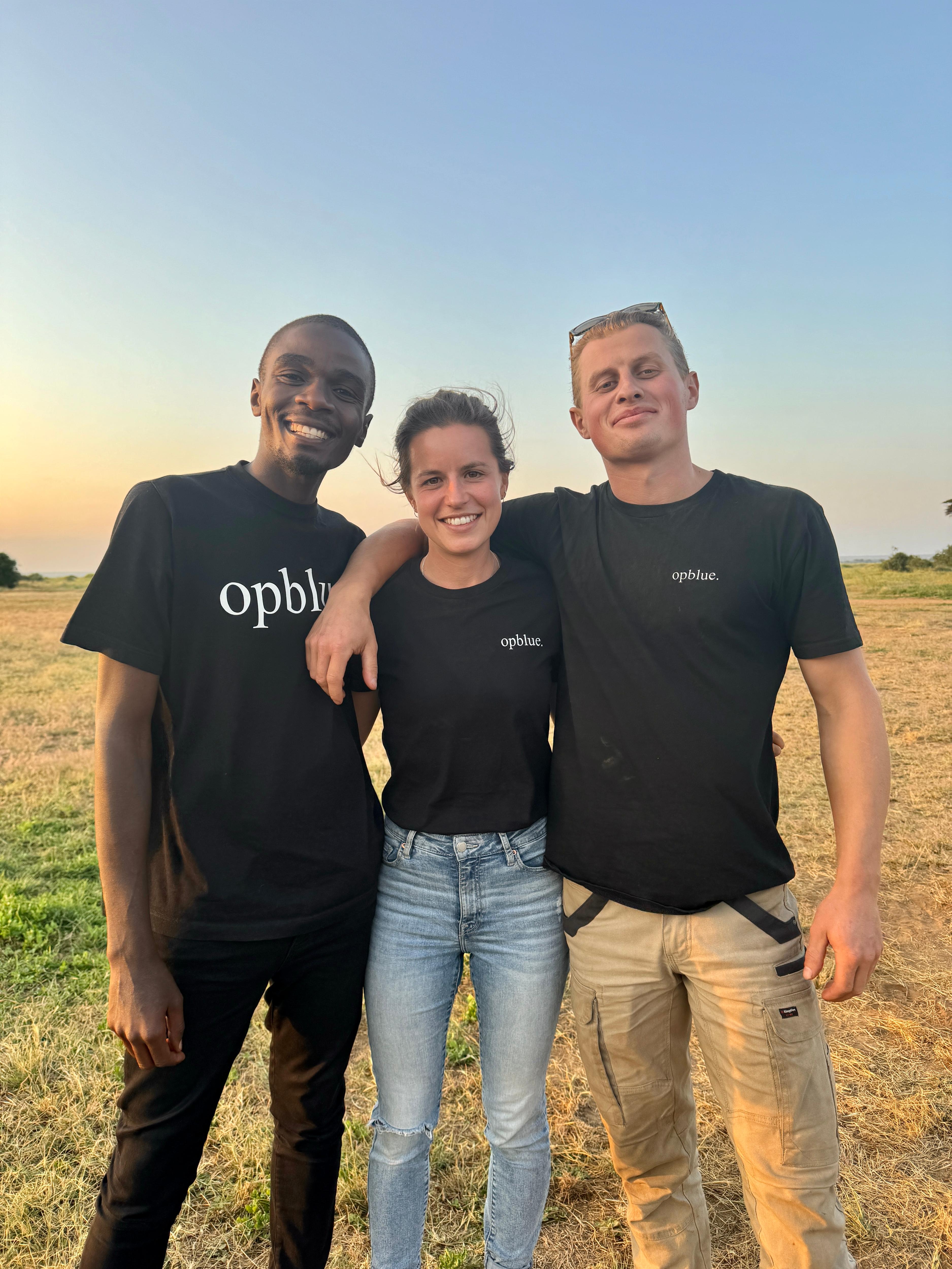 Three people smile with their hands around each other. 
