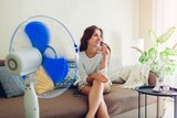 Smiling woman sitting on a couch in front of an oscillating fan, in a story about reducing mould and COVID spread at home.