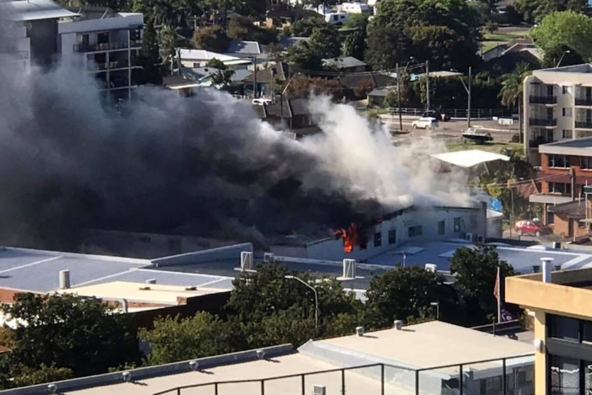 Flames and thick smoke are seen coming out of a large commercial building.