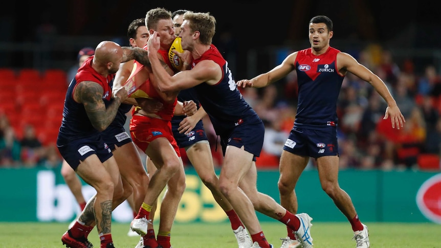 A cluster of Melbourne and Gold Coast players engage in a furious scramble for the football.