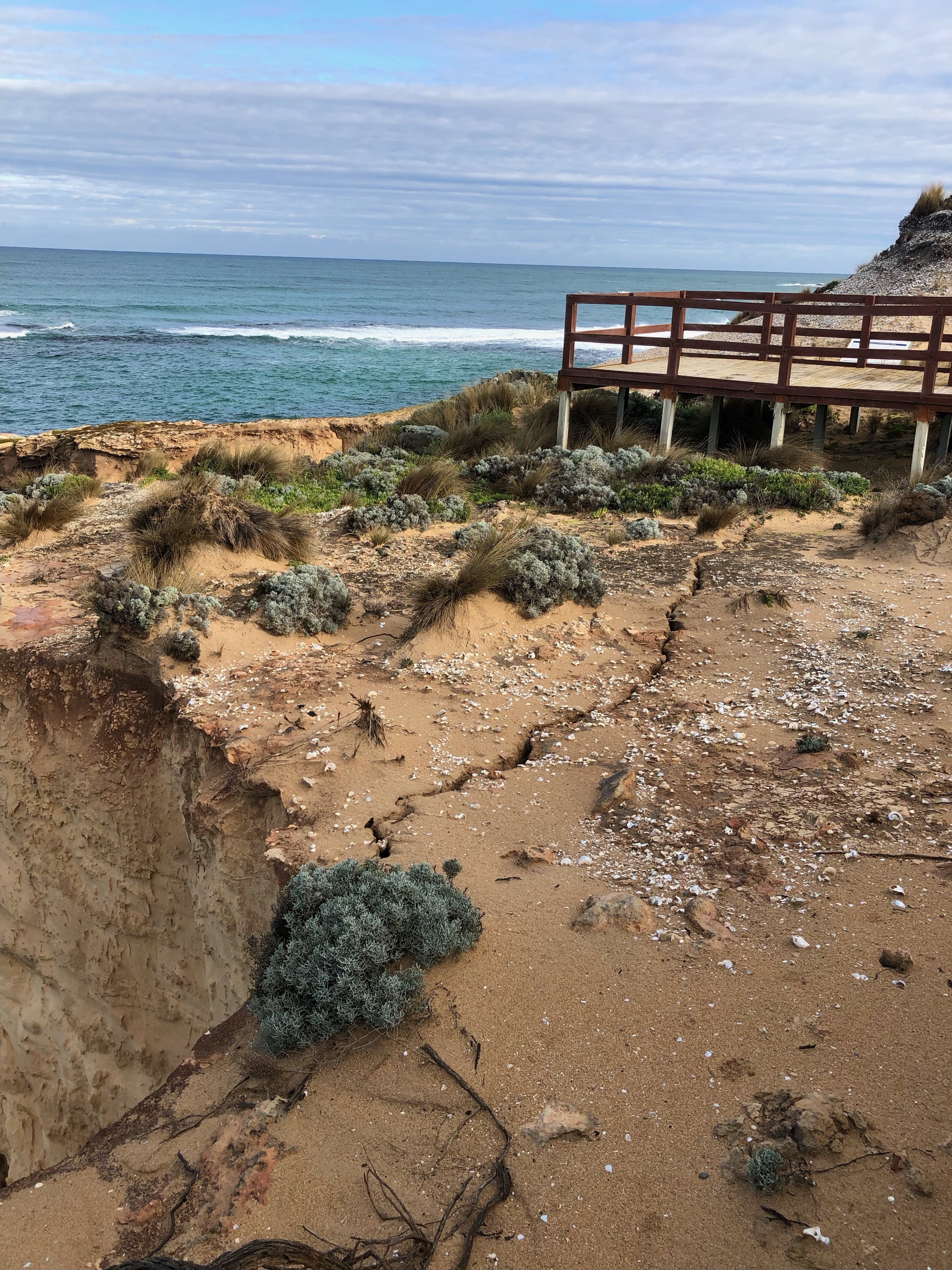 Large cracks running along the ground atop a limestone cliff with a viewing platform nearby