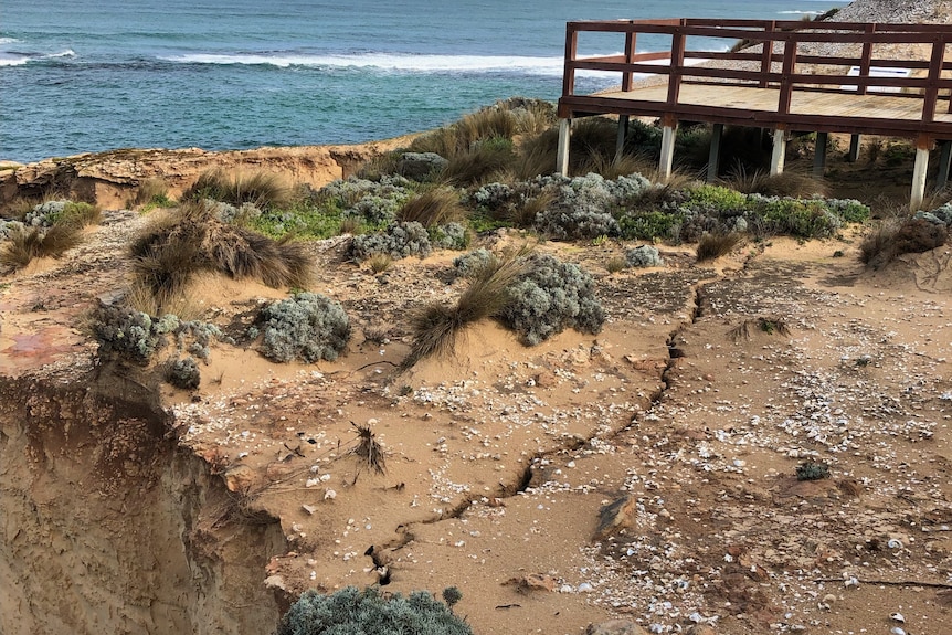 Large cracks running along the ground atop a limestone cliff with a viewing platform nearby