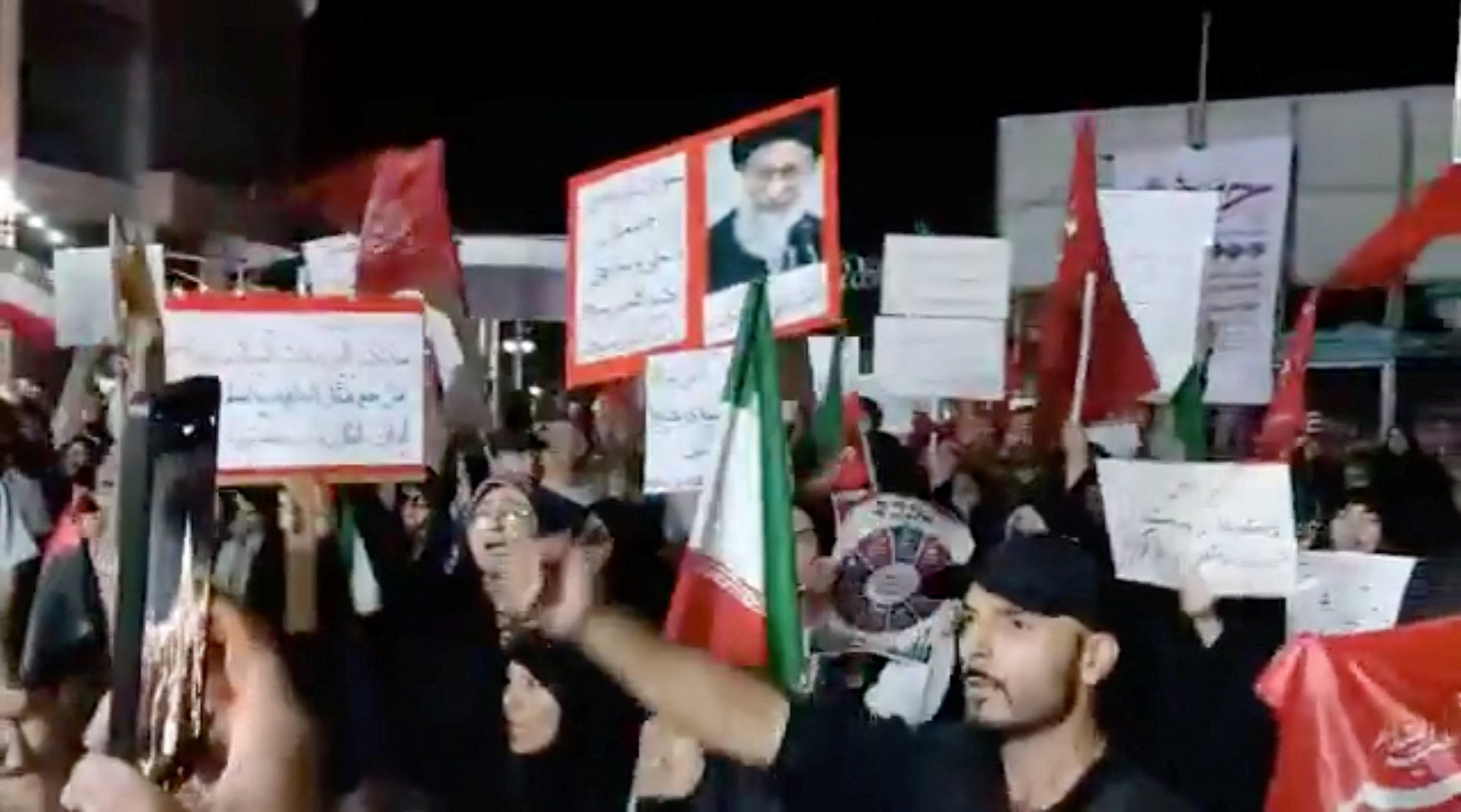 A group of people wearing black and holding Iranian flags, waving protest signs.