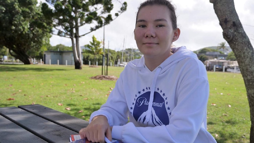 Chelsea Ajisaka, dark eyes and brown hair sits at a park table with her arms folded on top of her chemistry textbook.