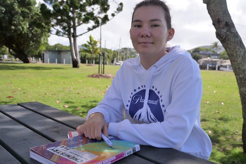 Chelsea Ajisaka, dark eyes and brown hair sits at a park table with her arms folded on top of her chemistry textbook.