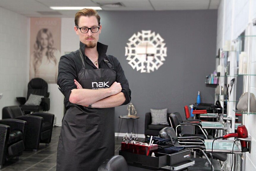 Man stands in salon wearing apron, glasses