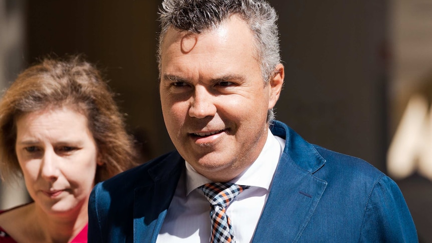 A head and shoulders shot of Steve Kaless smiling walking outside court wearing a suit and tie.