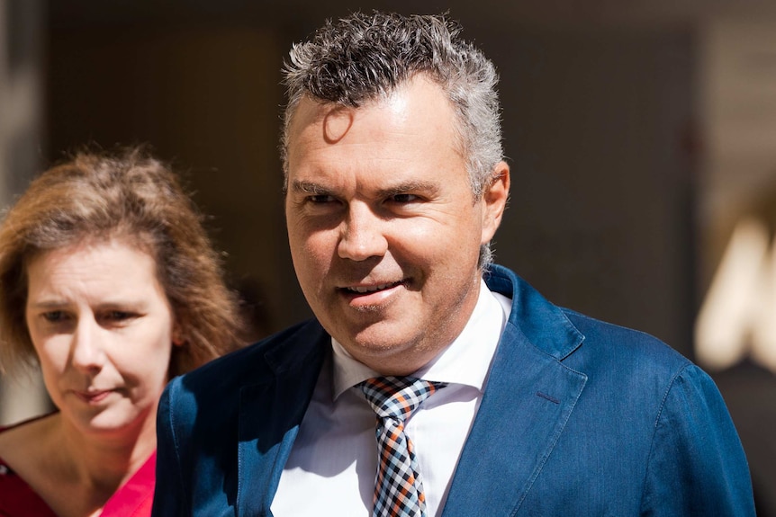 A head and shoulders shot of Steve Kaless smiling walking outside court wearing a suit and tie.