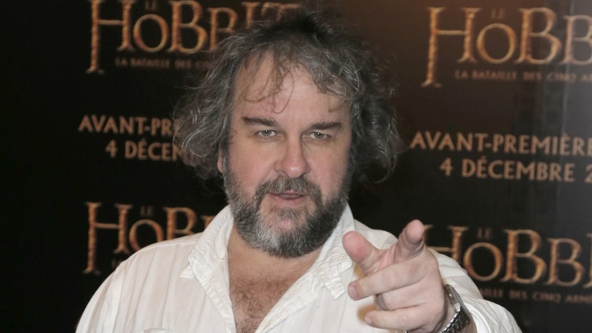 A man with long grey hair with beard points towards a camera