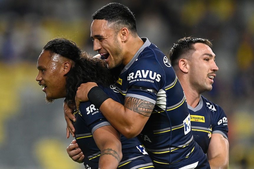 Luciano Leilua is hugged by Cowboys teammates Valentine Holmes and Reece Robson after a try against the Warriors.