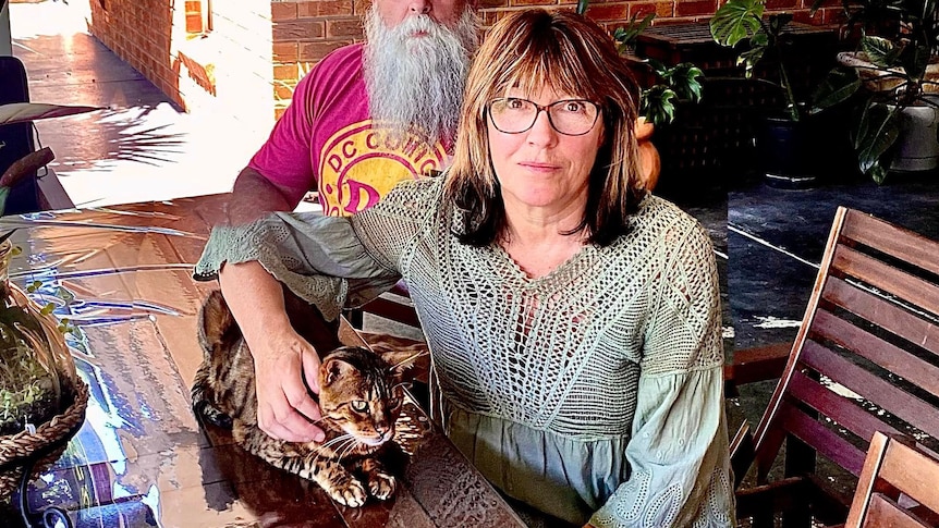 A woman in a grey crochet top cuddles her cat sitting on a table