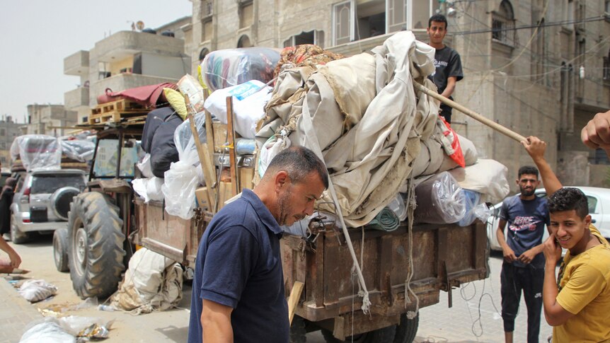 A man and three younger men move a trailer overflowing with goods wrapped in blankets.