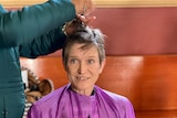 A woman getting her hair cut while a small terrier sits in her lap