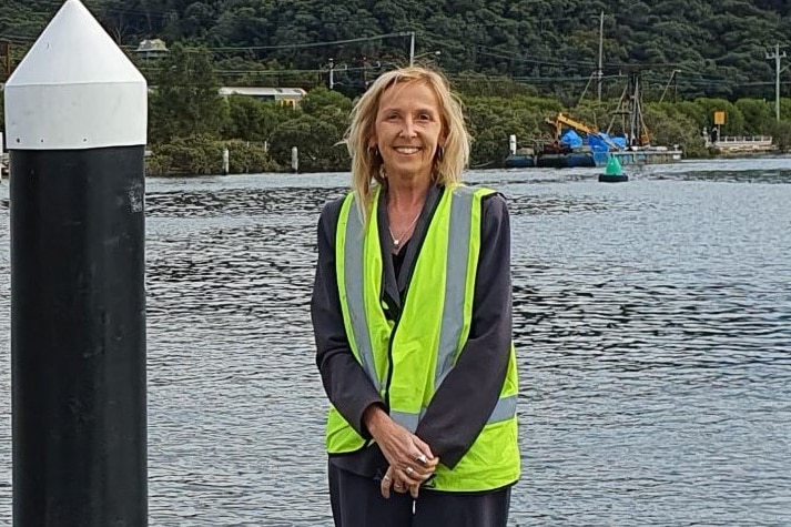 A smiling blonde woman in high-vis stands on a wharf.