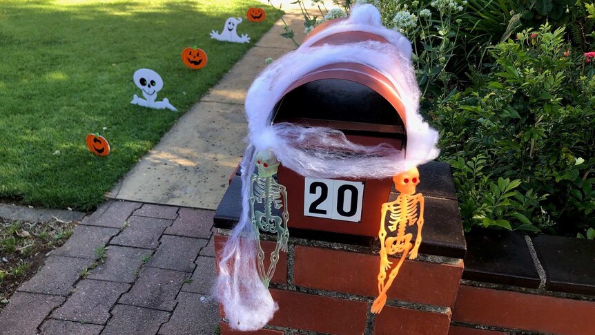 Fake cobwebs on a letterbox and other Halloween decorations in a front yard