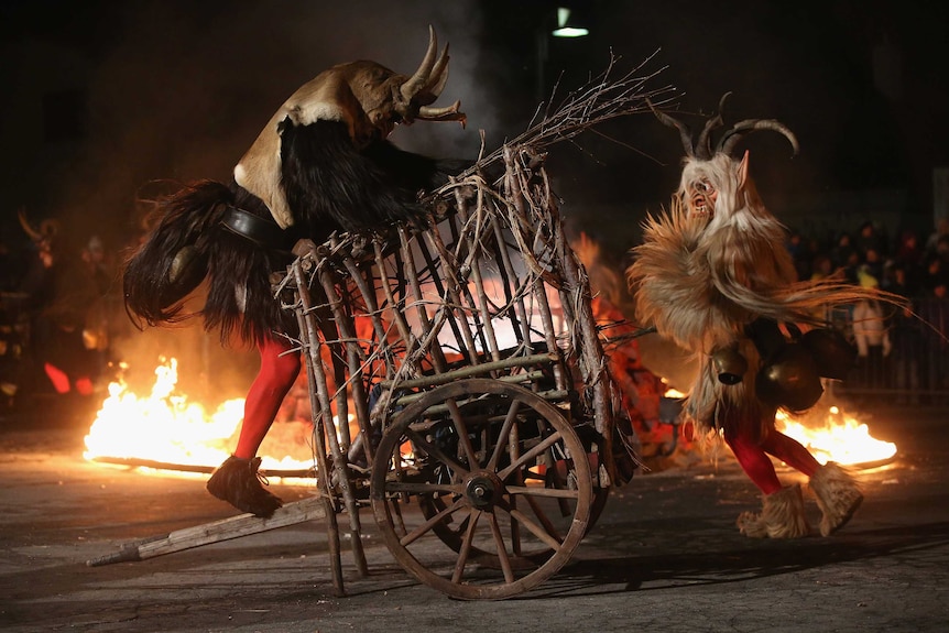 Two Krampus creatures attack a cart where a delinquent little boy is captive on the town square.