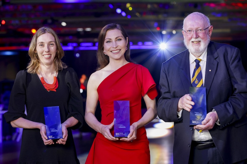 Three people pose with awards.
