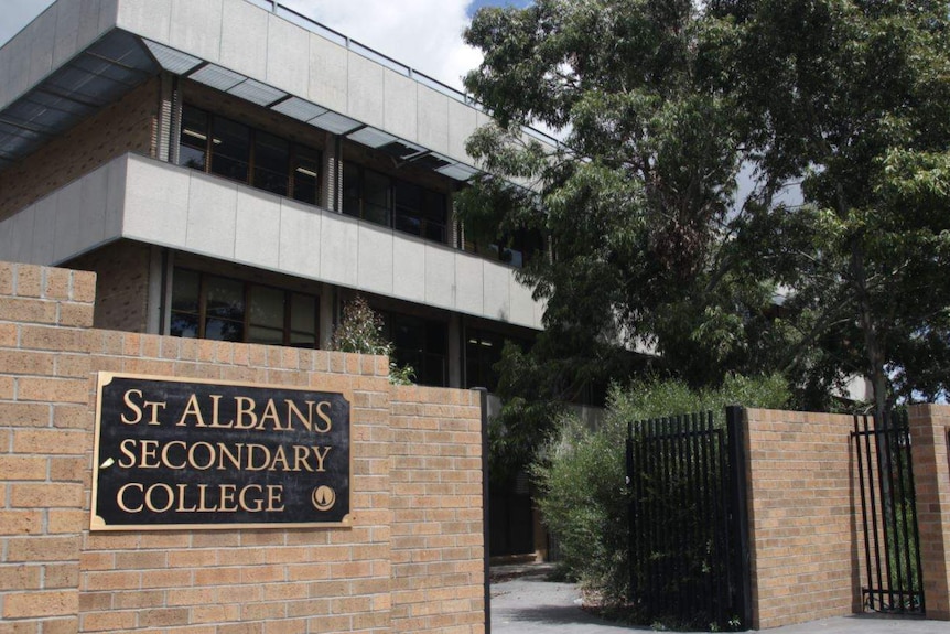 A brown brick building and fence with signs for St Albans Secondary College