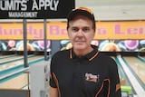 A man in a black and orange uniform stands in front of a bowling alley.