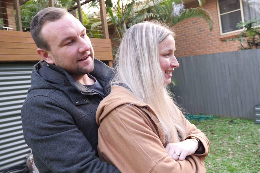 Man cuddling his wife from behind looking ahead in profile