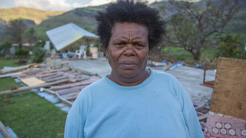 Woman looks concerned standing out front of cyclone-damaged buildings