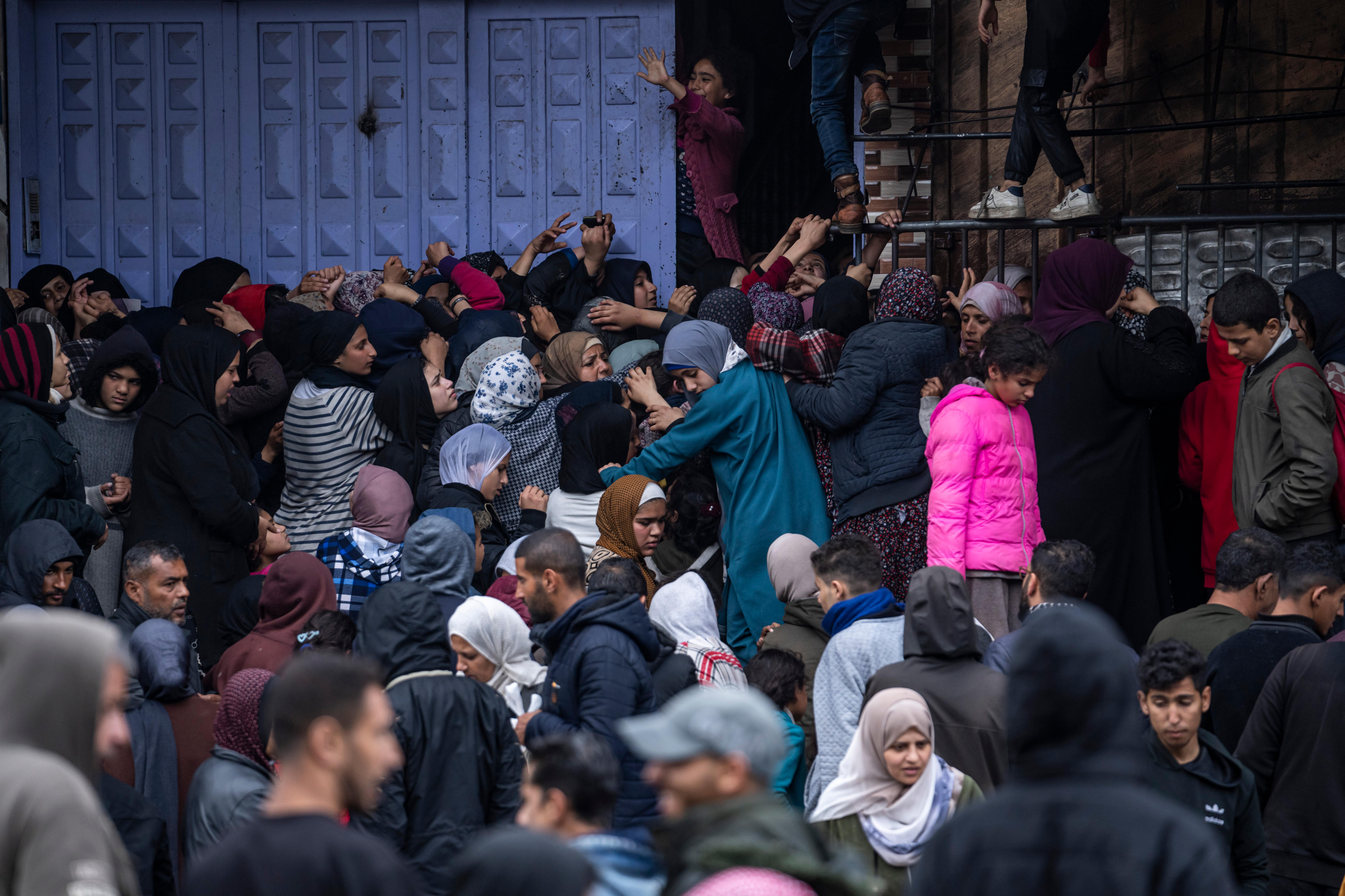 A crowd of young women and girls pack in extremely tightly to a doorway, some reaching out their hands.