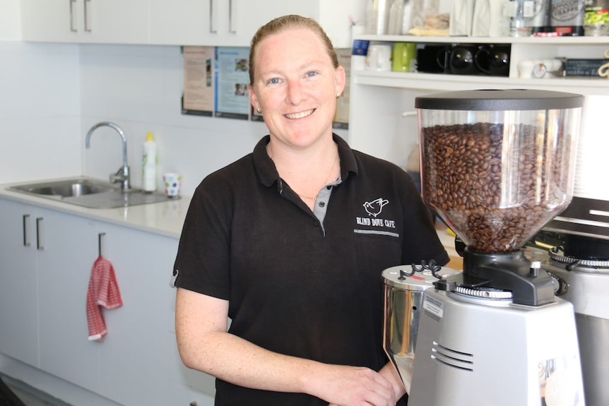 A lady dressed in a polo t-shirt stands in front of a coffee machine.