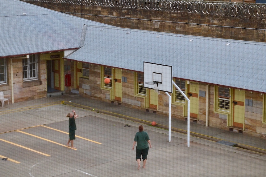 Inmates pay basketball inside the Berrima Correctional Centre, looking down through fencing above the court.