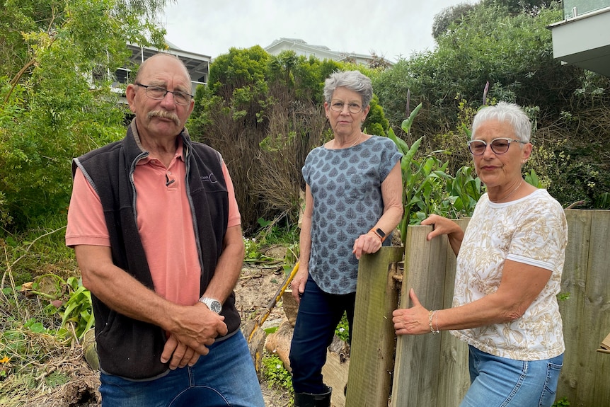 One man and two women look disappointed as they stand next to a timber fence.