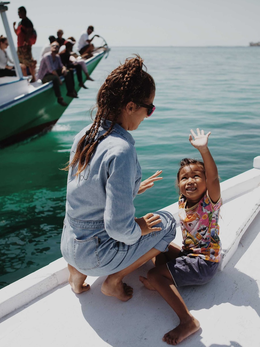 A woman plays with a toddler on the bow of a boat.