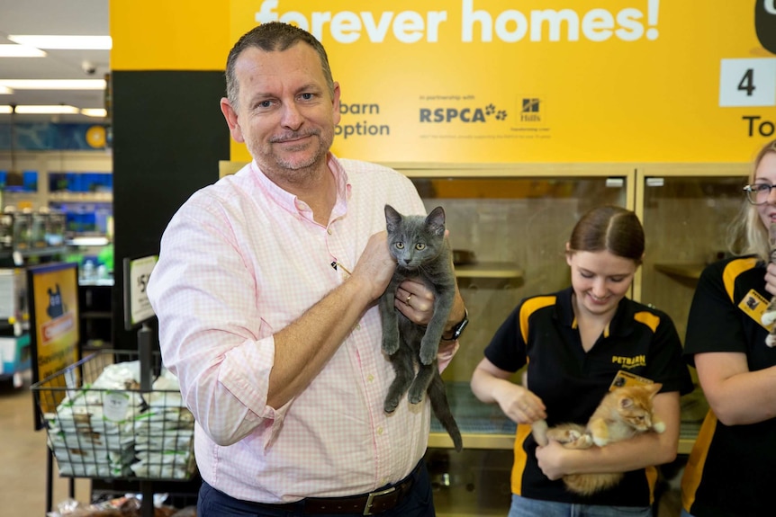 A man holds a cat in a Petbarn store.