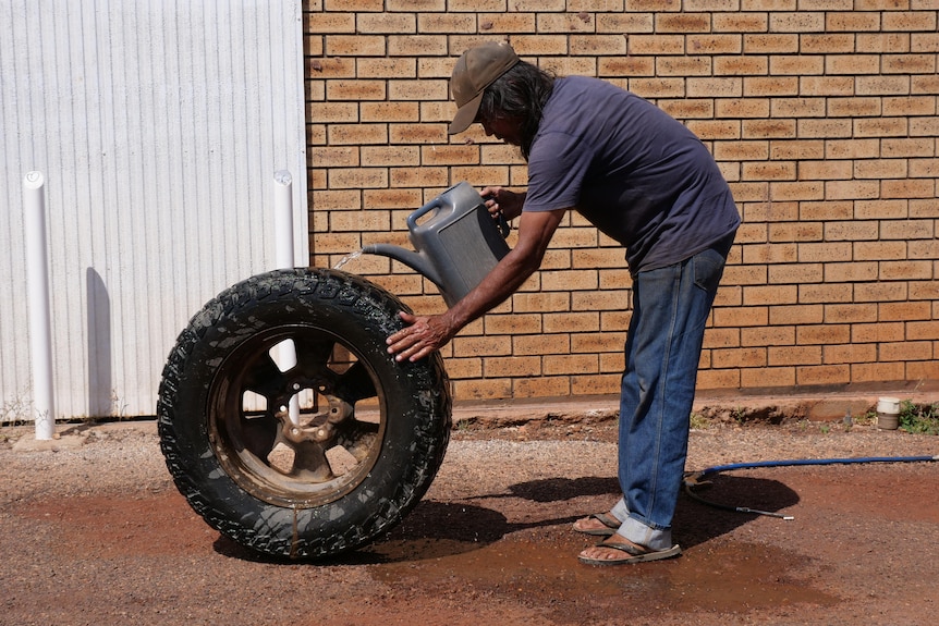 An Indigenous man pours water over a large tyre in the street