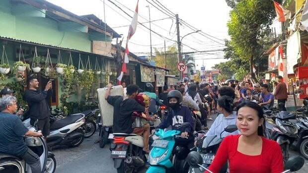 A man holds a large figurine head while riding through traffic on a scooter