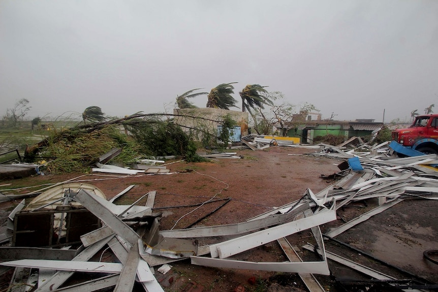 Damaged structures and uprooted tress lie along a road that was hit by a powerful storm