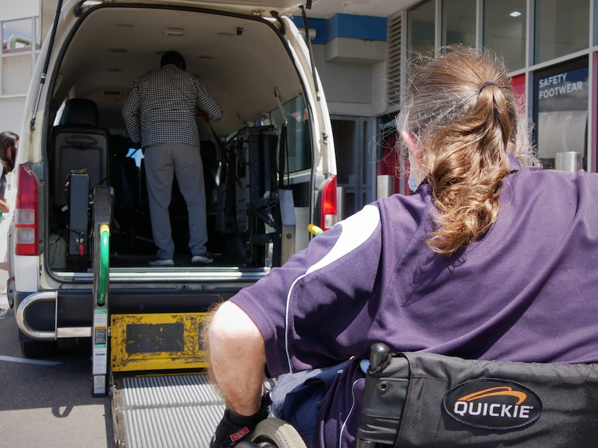 A man in a in a wheelchair waiting to enter a maxi taxi.