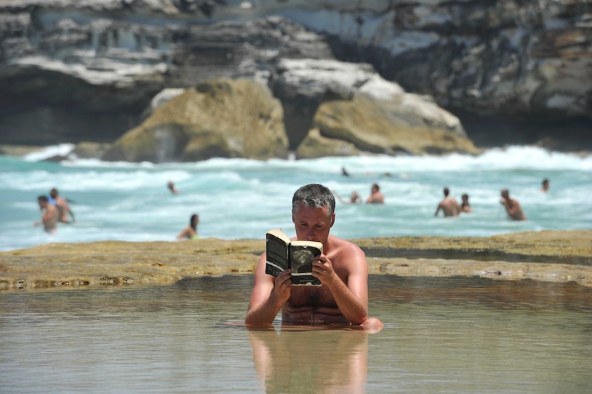 Man reads a book in the water at Tamarama Beach
