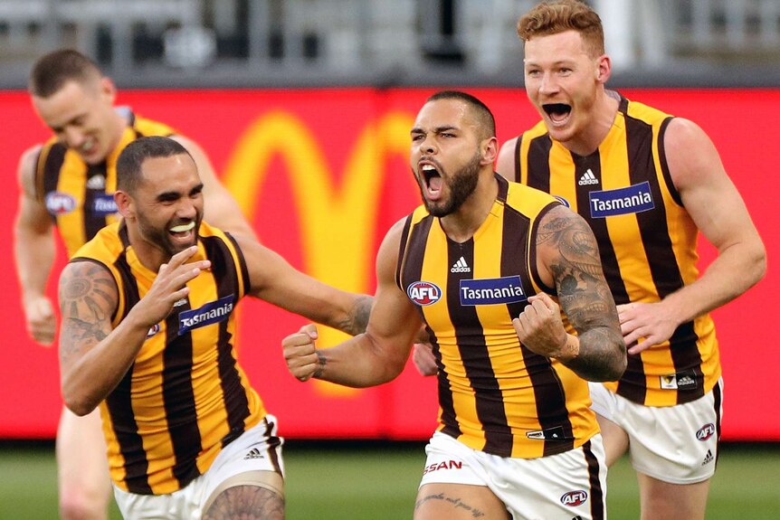 An AFL footballer pumps his fists and roars as he runs after scoring, while teammates celebrate.
