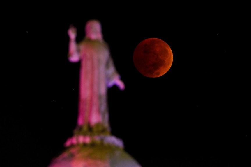 The moon and a statue are seen during a lunar eclipse in San Salvador, El Salvador