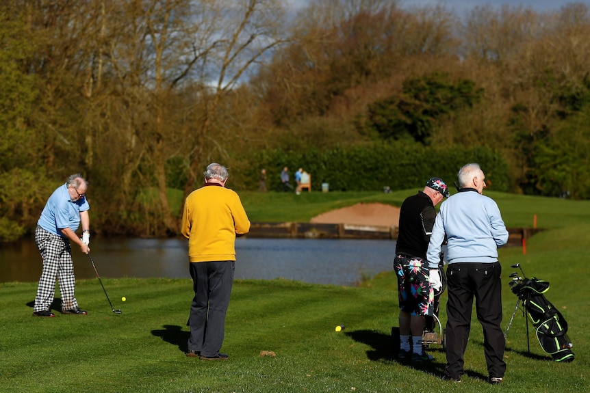 Four elderly golfer stand on the tee of an attractive golf course on a spring day.