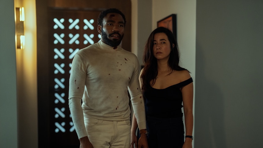 A black man and a Japanese woman stand next to each other. They look disheveled and unhappy