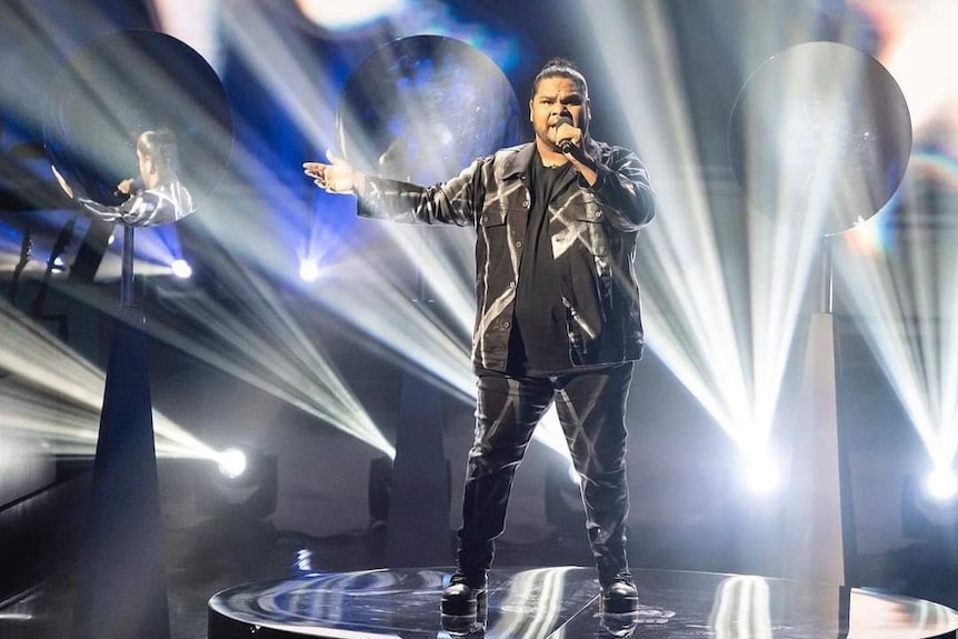 A man singing on a brilliantly lit stage in a TV studio.