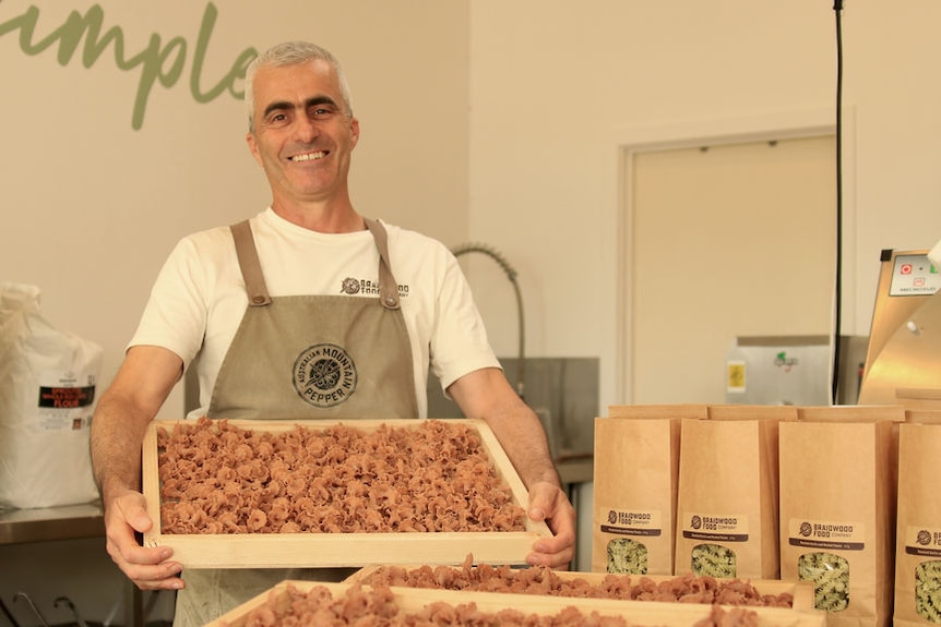 A man smiles as he holds a tray of flavoured pasta.