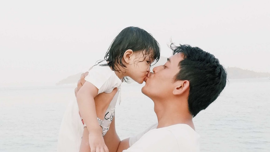 Dad lifting up and kissing his toddler with the ocean in the background.