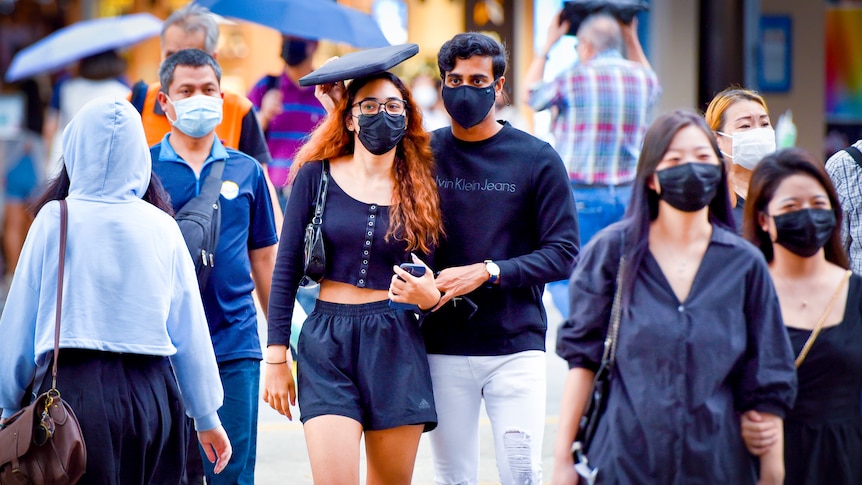 A young masked man holds a folder over a masked young woman's head as they cross a street 