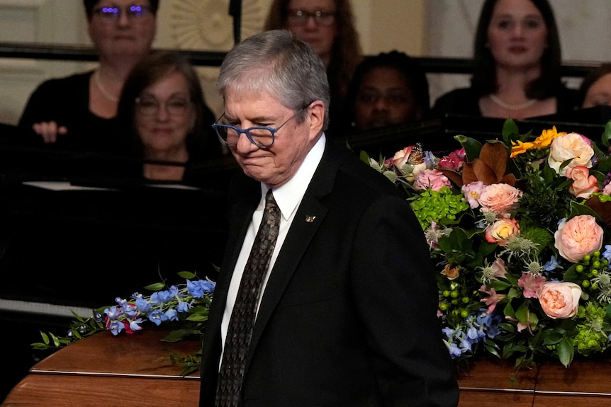 James "Chip" Carter in front of a casket covered in flowers. 